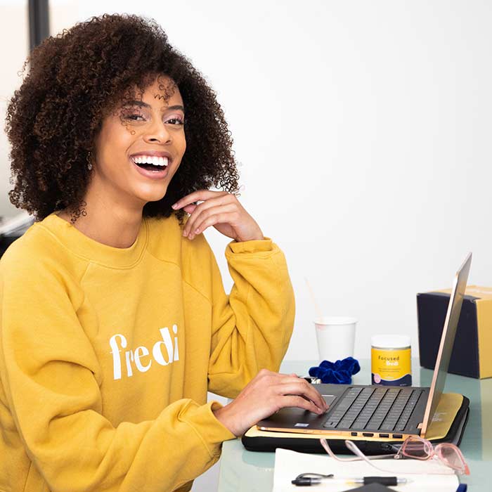 woman in yellow sweatshirt sitting in front of a laptop at a desk