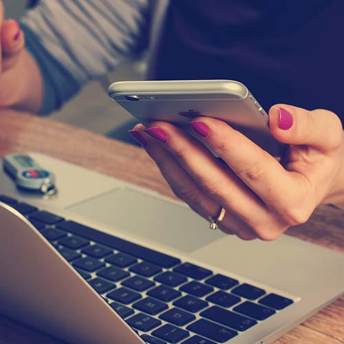 hand holding a cellphone in front of a laptop