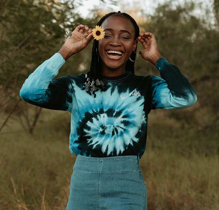 Laughing girl in jeans and tie-dyed shirt holding a yellow daisy