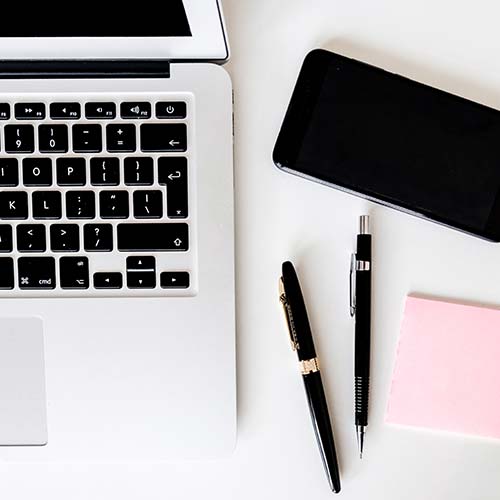 birds eye view of a table with a laptop, phone, notepad and pens on it