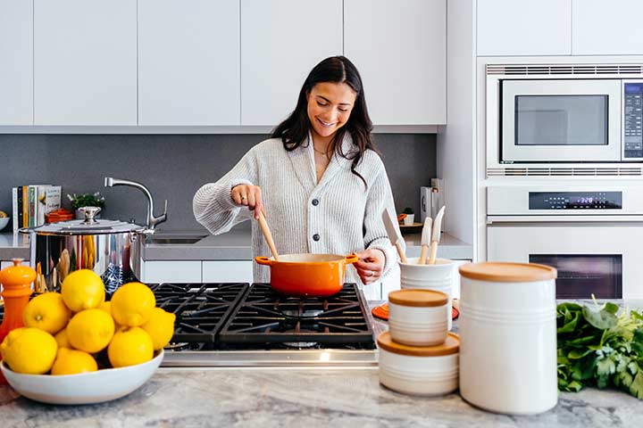 Woman stirring an orange pot with a wooden spoon over a gas hob in a modern kitchen